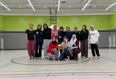 The volleyball drop-in group posing under the net in a gym
